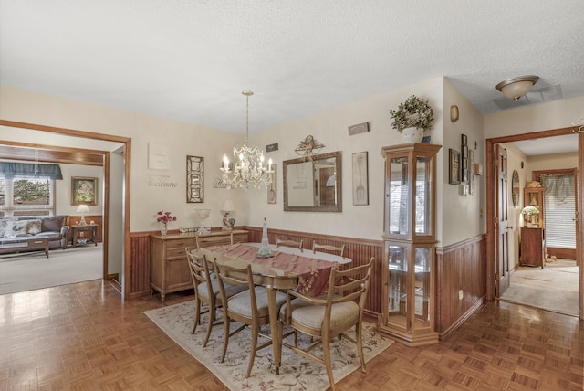 dining room with a notable chandelier, a textured ceiling, wood walls, and wainscoting