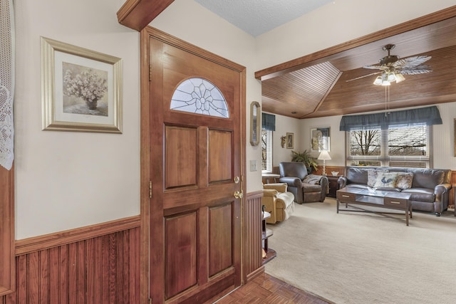 carpeted entrance foyer featuring a wainscoted wall, lofted ceiling, ceiling fan, and wooden ceiling