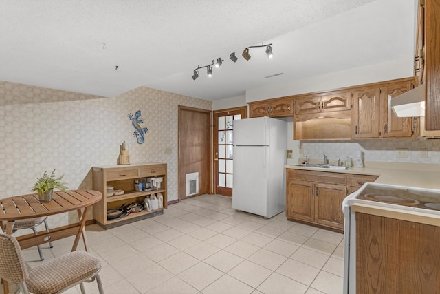 kitchen with a sink, wallpapered walls, white appliances, wall chimney range hood, and light countertops