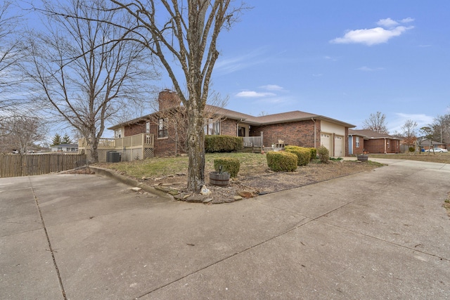 view of front of house with central AC unit, driveway, an attached garage, a chimney, and brick siding