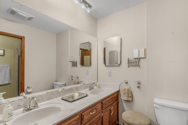 full bathroom with a sink, visible vents, toilet, and a textured ceiling