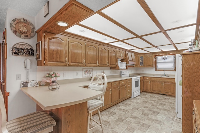 kitchen featuring a kitchen breakfast bar, white appliances, a peninsula, brown cabinetry, and light countertops