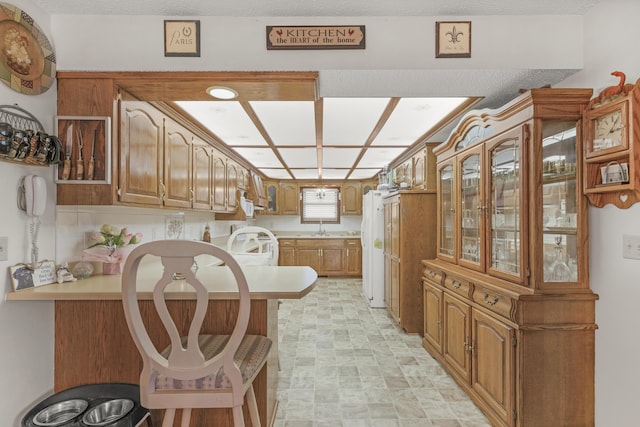 kitchen featuring a peninsula, light countertops, glass insert cabinets, a kitchen breakfast bar, and brown cabinets