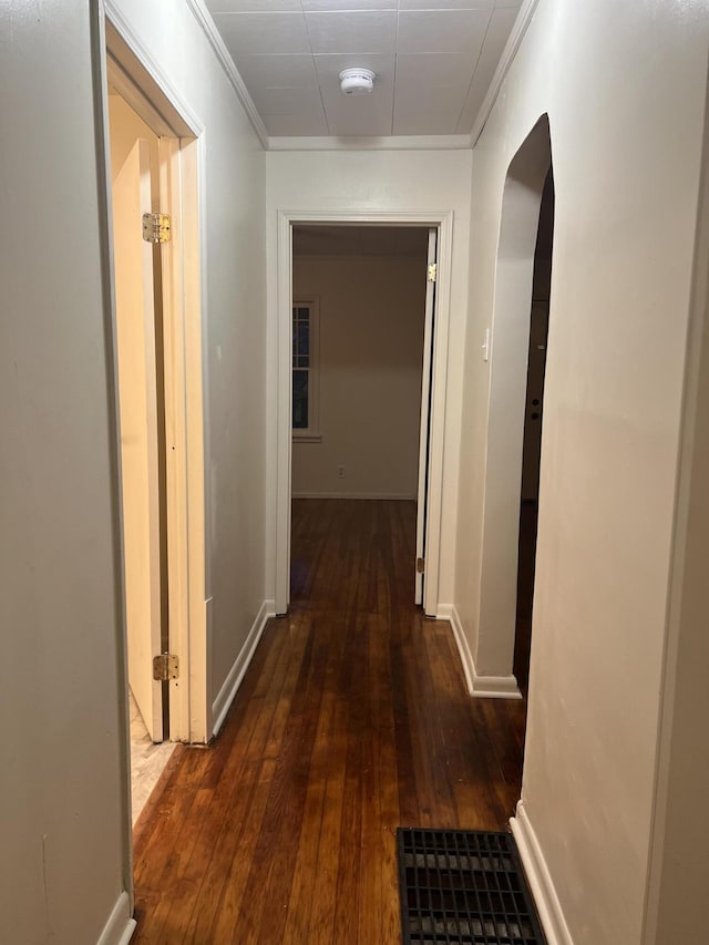 hallway with ornamental molding, dark wood-type flooring, arched walkways, and baseboards