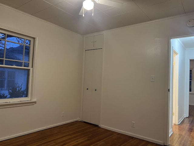 unfurnished bedroom with a closet, baseboards, dark wood finished floors, and crown molding