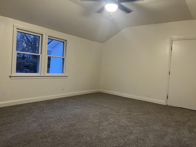 spare room with dark colored carpet, vaulted ceiling, baseboards, and ceiling fan