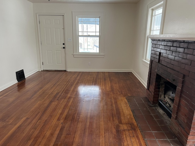 unfurnished living room with a brick fireplace, baseboards, and dark wood-type flooring