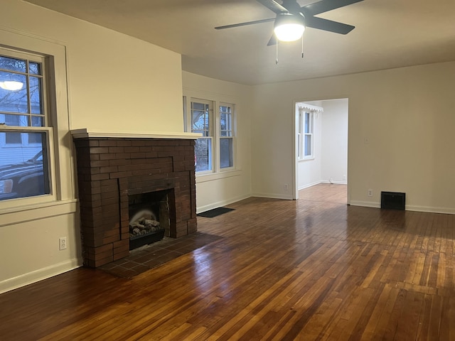 unfurnished living room featuring dark wood-type flooring, a brick fireplace, and baseboards