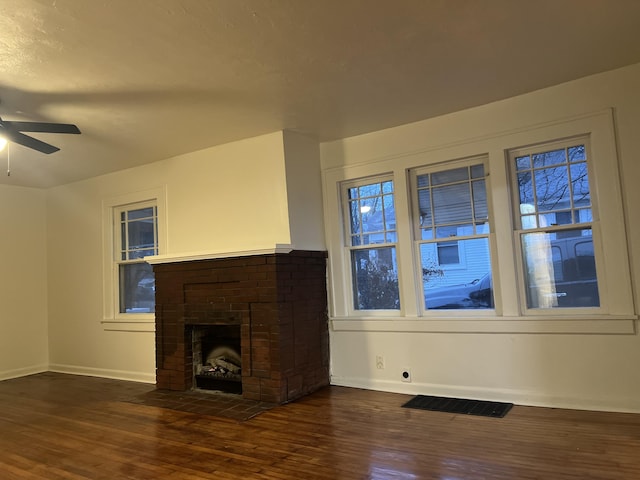 unfurnished living room featuring dark wood-type flooring, a brick fireplace, visible vents, and a ceiling fan