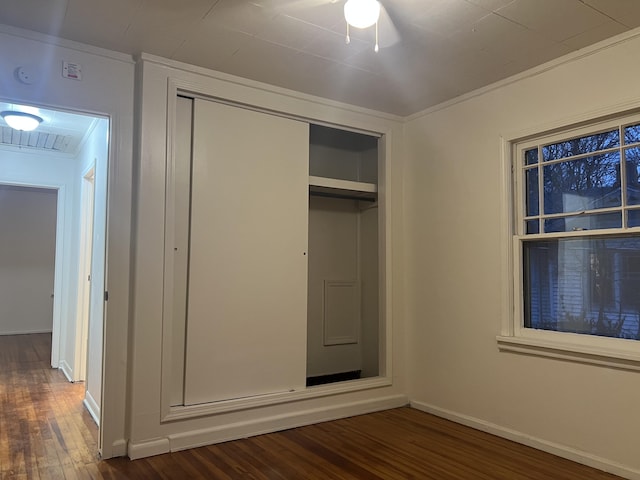 unfurnished bedroom featuring dark wood-style floors, a closet, baseboards, and crown molding