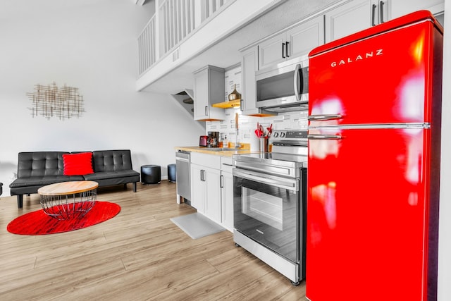 kitchen with tasteful backsplash, a high ceiling, appliances with stainless steel finishes, a sink, and light wood-type flooring