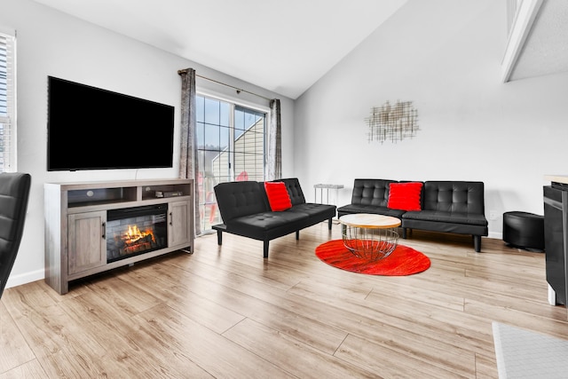 living room with high vaulted ceiling, light wood-style flooring, baseboards, and a glass covered fireplace