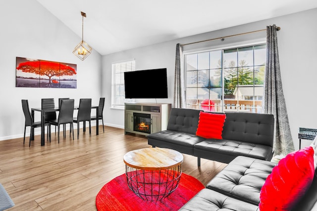 living room with lofted ceiling, a glass covered fireplace, baseboards, and wood finished floors