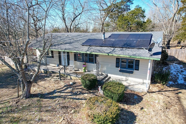 ranch-style house featuring solar panels, a porch, a shingled roof, and fence