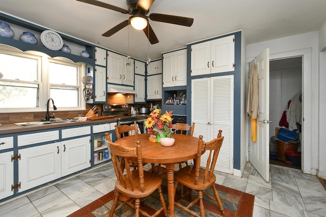 kitchen with dark countertops, stainless steel electric range oven, under cabinet range hood, white cabinetry, and a sink