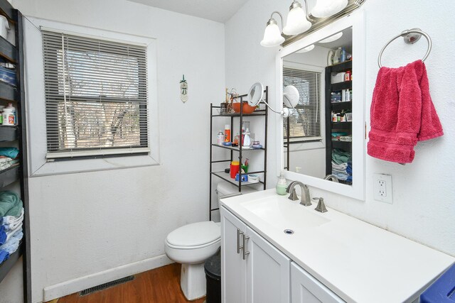 half bathroom with toilet, wood finished floors, vanity, visible vents, and baseboards