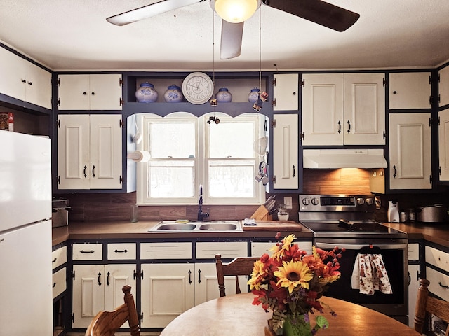 kitchen featuring dark countertops, freestanding refrigerator, a sink, under cabinet range hood, and stainless steel electric range