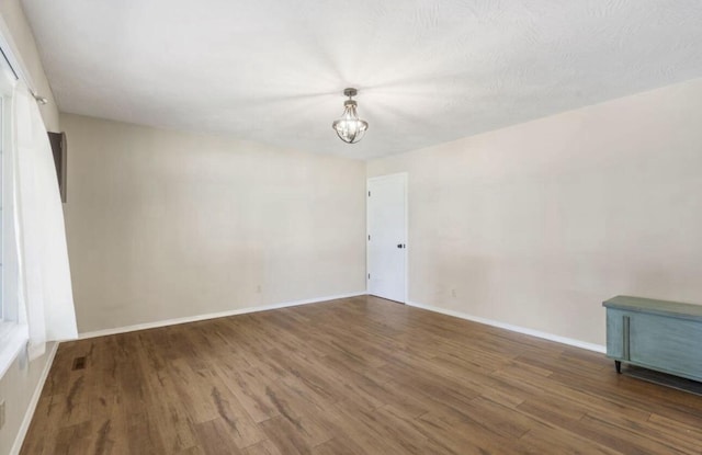 spare room with visible vents, baseboards, a chandelier, and dark wood-style flooring