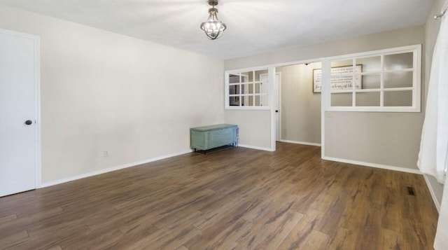 spare room featuring dark wood-style floors, visible vents, baseboards, and a notable chandelier