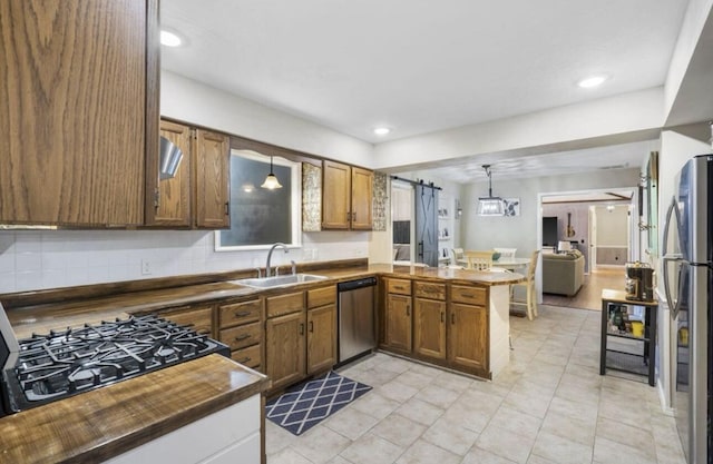 kitchen with a barn door, stainless steel appliances, a sink, dark countertops, and pendant lighting