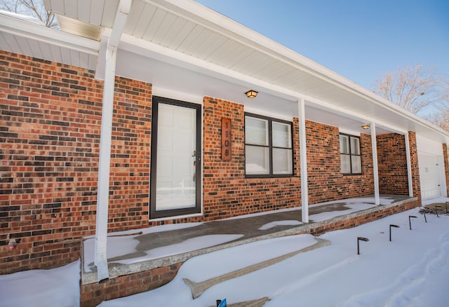 snow covered property entrance featuring brick siding