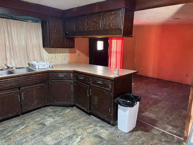 kitchen with light countertops, a peninsula, a sink, and dark brown cabinetry