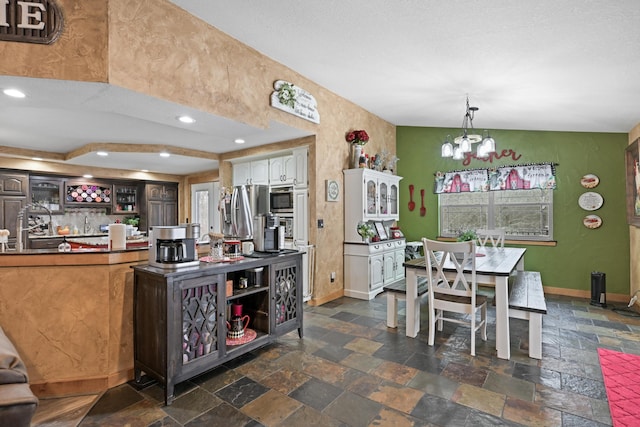 kitchen featuring baseboards, white cabinets, hanging light fixtures, and stone tile floors