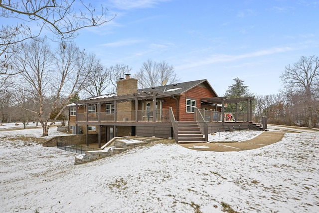 snow covered back of property with a chimney, stairway, and a wooden deck