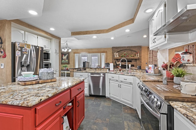 kitchen with white cabinets, a raised ceiling, wall chimney exhaust hood, stainless steel appliances, and light countertops