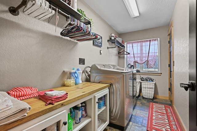 washroom with laundry area, baseboards, a textured wall, stone tile flooring, and separate washer and dryer