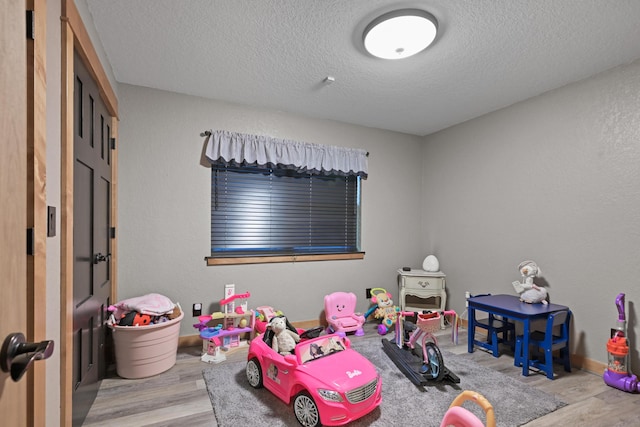 rec room with light wood finished floors, baseboards, a textured ceiling, and a textured wall