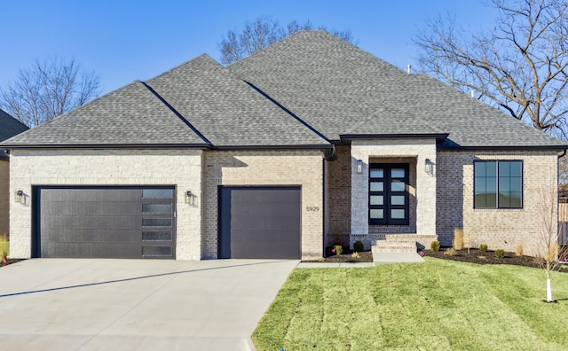 french country style house featuring an attached garage, brick siding, roof with shingles, and a front yard