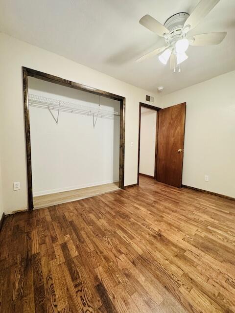 unfurnished bedroom with baseboards, visible vents, a ceiling fan, wood finished floors, and a closet