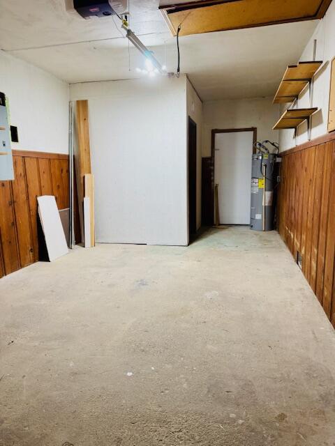 below grade area featuring a garage, wainscoting, electric water heater, and wood walls