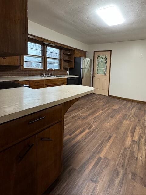 kitchen featuring dark wood-style flooring, freestanding refrigerator, light countertops, open shelves, and a sink