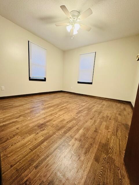 empty room with a textured ceiling, light wood finished floors, a ceiling fan, and baseboards