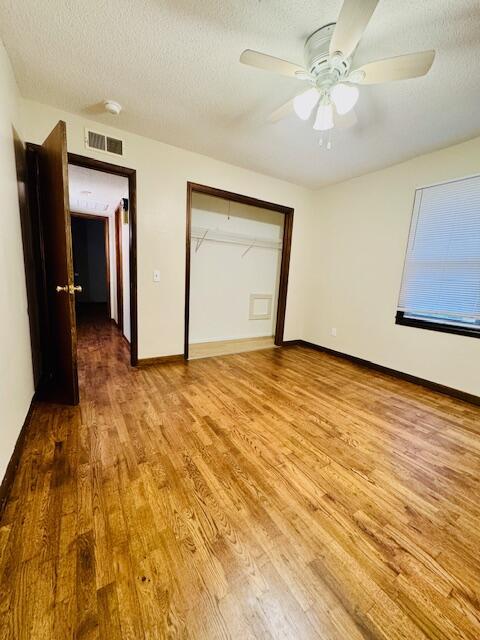 unfurnished bedroom with a textured ceiling, visible vents, baseboards, a closet, and light wood finished floors