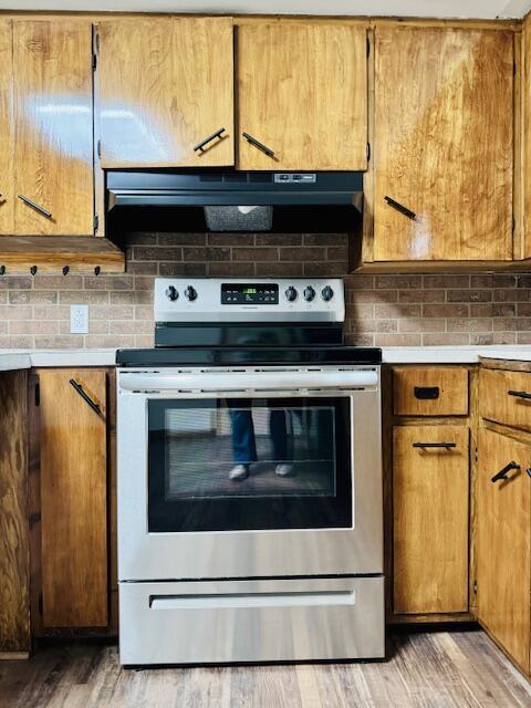 kitchen with under cabinet range hood, tasteful backsplash, light countertops, and stainless steel range with electric cooktop