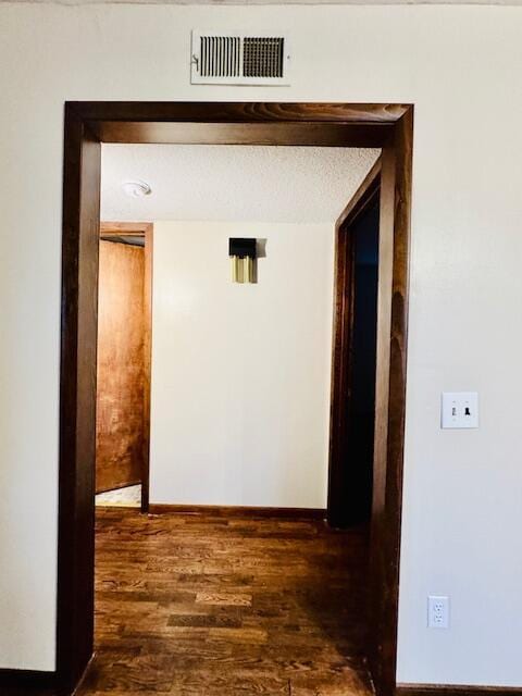 hall featuring visible vents, dark wood finished floors, a textured ceiling, and baseboards