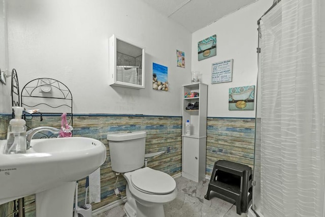 bathroom featuring curtained shower, toilet, a sink, marble finish floor, and wainscoting