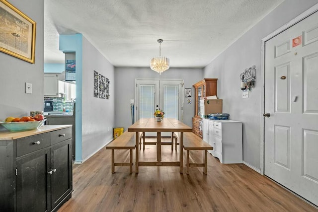 dining area with french doors, light wood finished floors, a textured ceiling, a chandelier, and baseboards