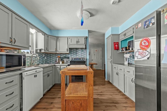 kitchen featuring stainless steel appliances, a sink, under cabinet range hood, and gray cabinetry