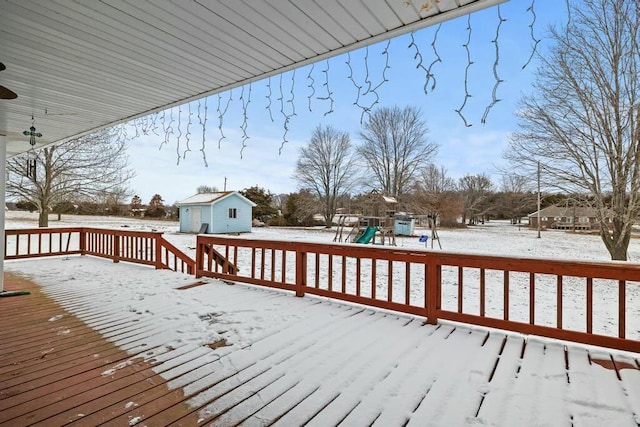 snow covered deck with an outbuilding, a playground, and a storage shed