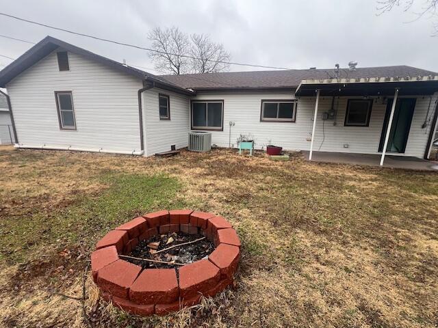 back of property with central AC unit, a fire pit, a lawn, and a patio