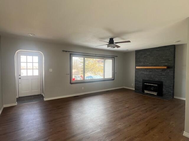 unfurnished living room featuring a healthy amount of sunlight, dark wood-style floors, and a stone fireplace