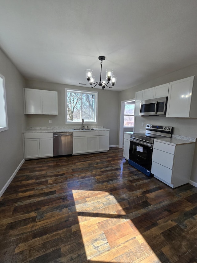 kitchen with appliances with stainless steel finishes, light countertops, white cabinets, and a notable chandelier