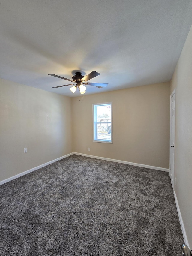 spare room with baseboards, dark carpet, and ceiling fan