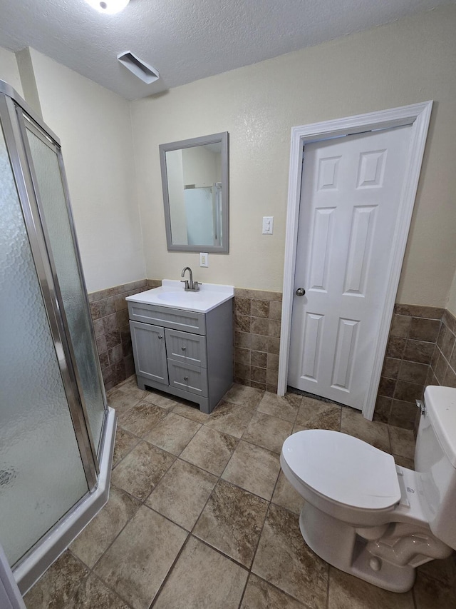 full bathroom featuring a wainscoted wall, tile walls, toilet, vanity, and a textured ceiling