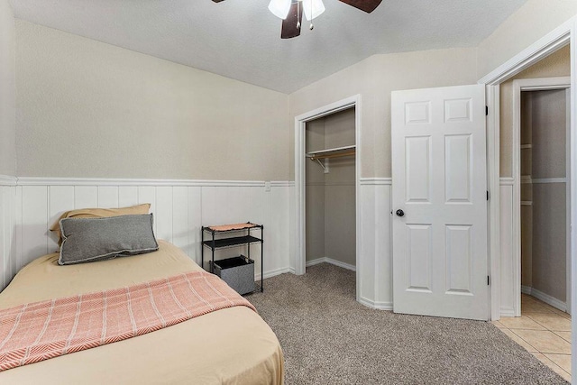 bedroom with lofted ceiling, a wainscoted wall, light tile patterned floors, and a closet