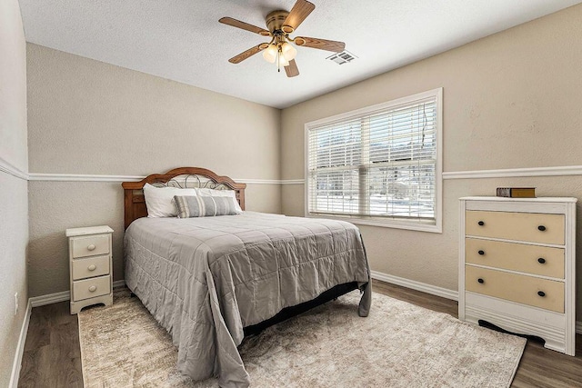 bedroom featuring baseboards, visible vents, wood finished floors, and a textured wall